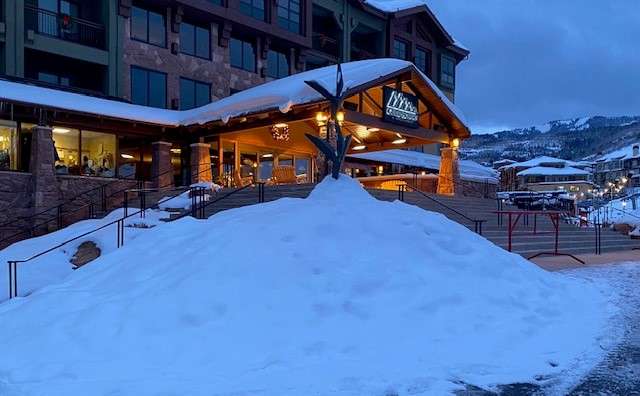 Cozy wooden lodge entrance covered in snow during twilight.