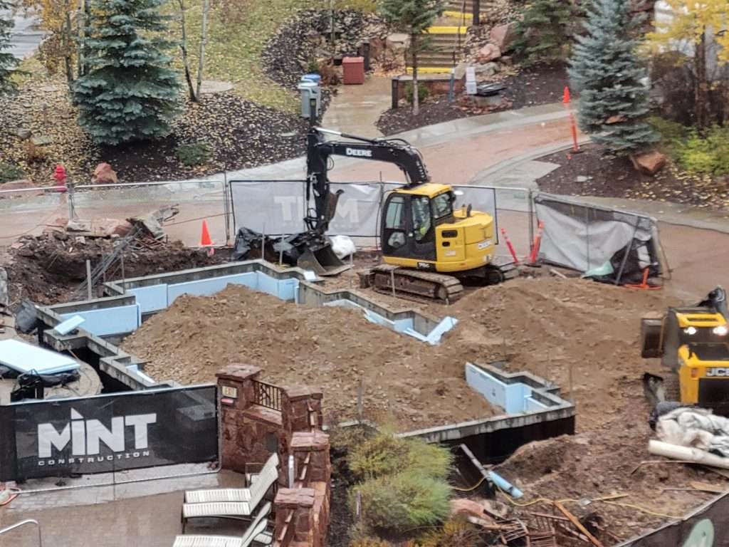 Excavator digging a backyard pond surrounded by landscaping.