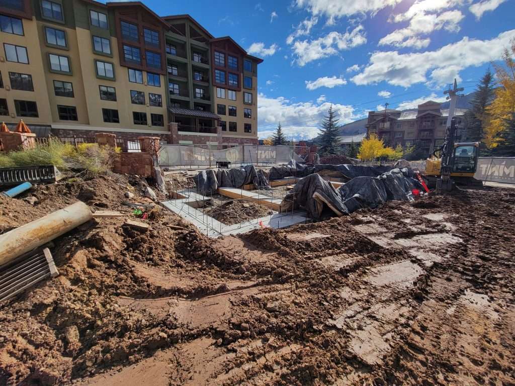Construction site with muddy ground and building foundations under a blue sky.