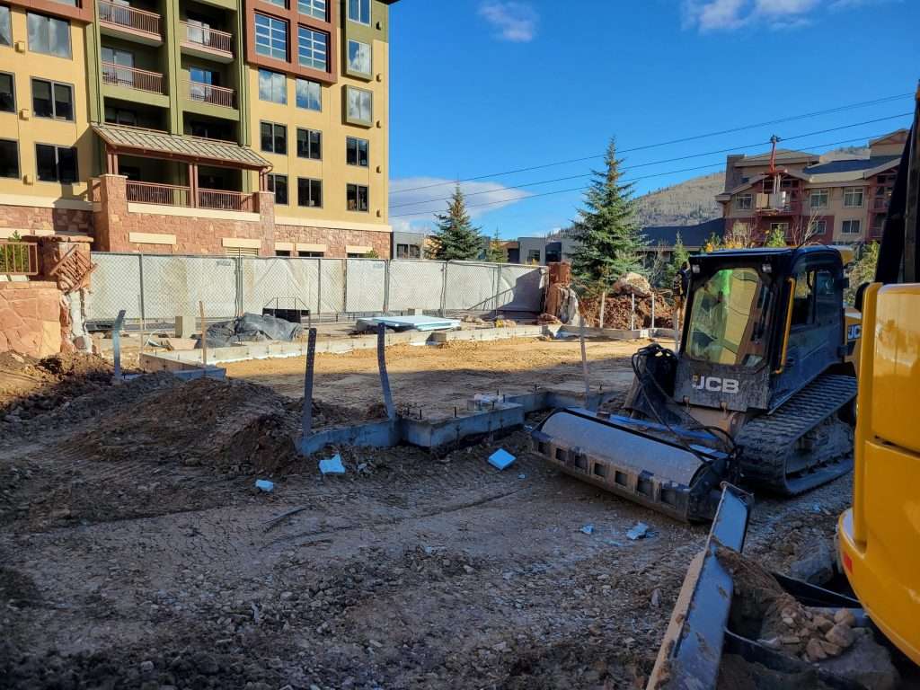 Construction site with machinery and building materials under a clear blue sky.