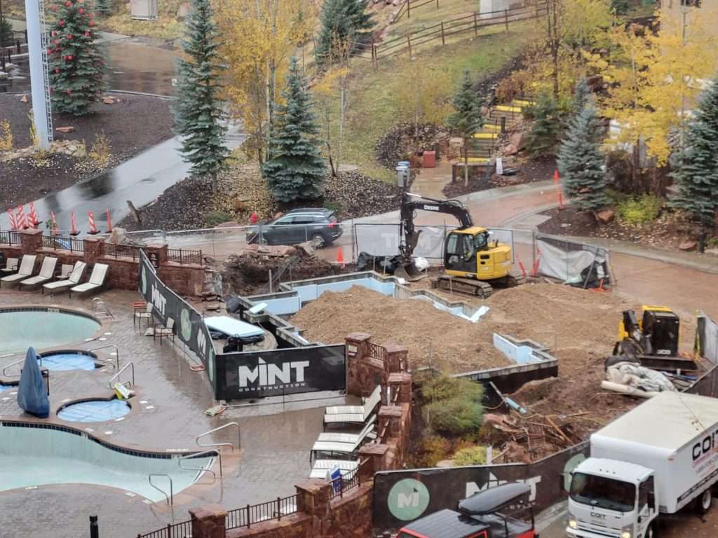Construction site with excavators and materials in a wooded area.