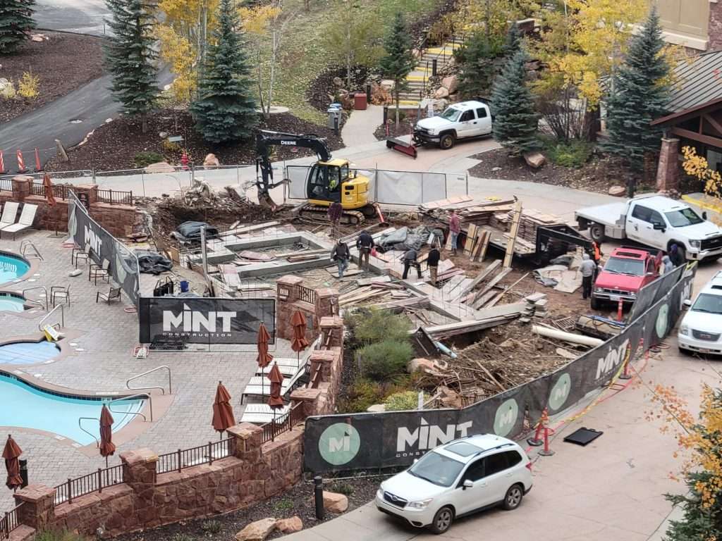Outdoor construction site with vehicles and workers amidst trees.