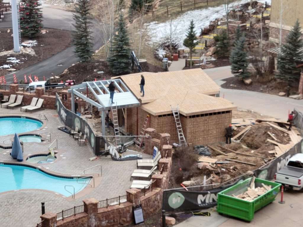 A large RV parked beside a pool with beige shade covering part of the area.