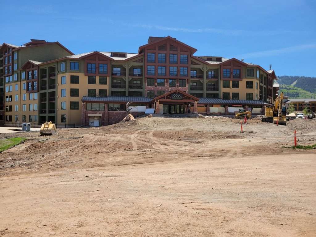 A large building under construction with dirt and construction materials in front.