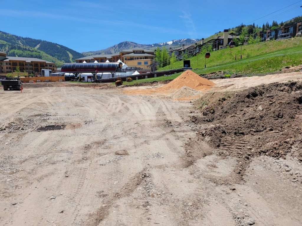 Construction site with dirt piles and buildings in a mountainous area.