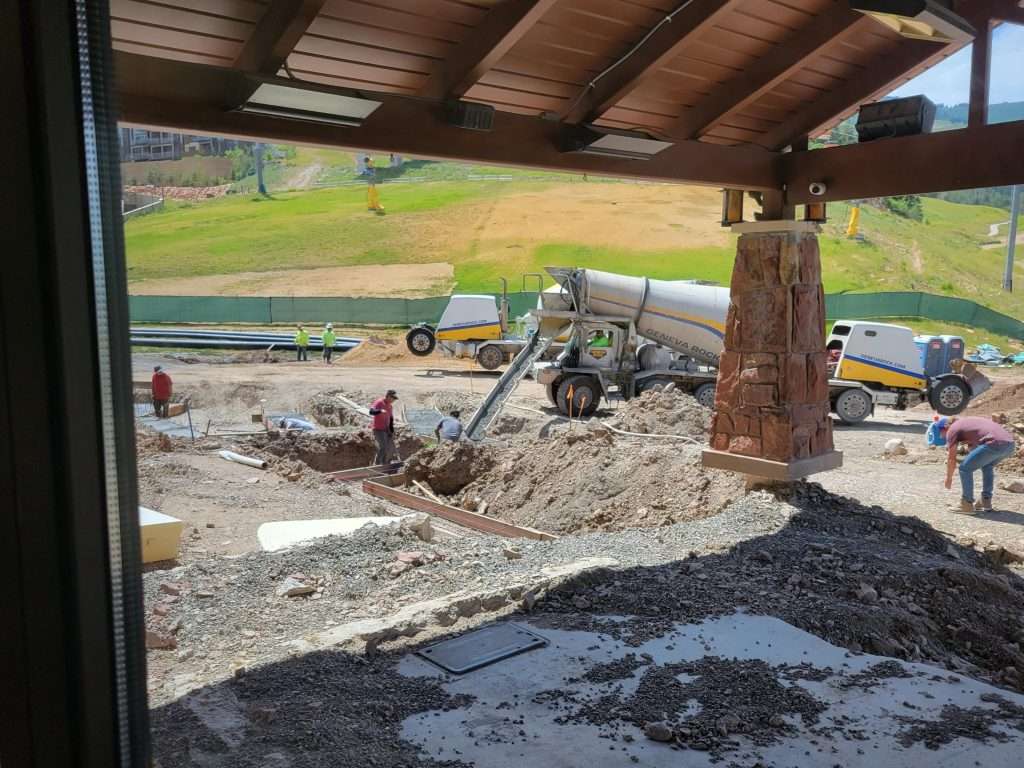 Construction site with heavy machinery and workers digging under a wooden roof.