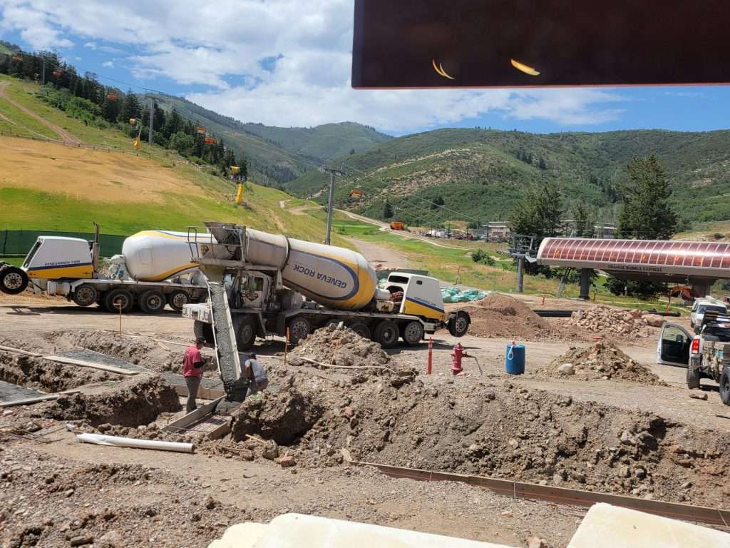 Excavator working on a rural construction site with hills in the background.