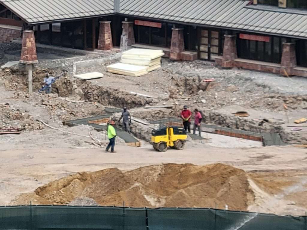 Construction workers operate machinery on a building site with exposed foundation work.