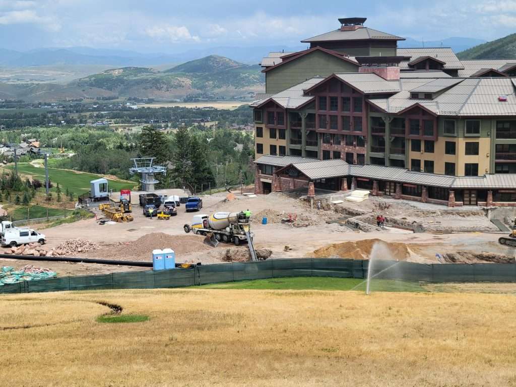 A large building under construction near a grassy field and mountains in the background.