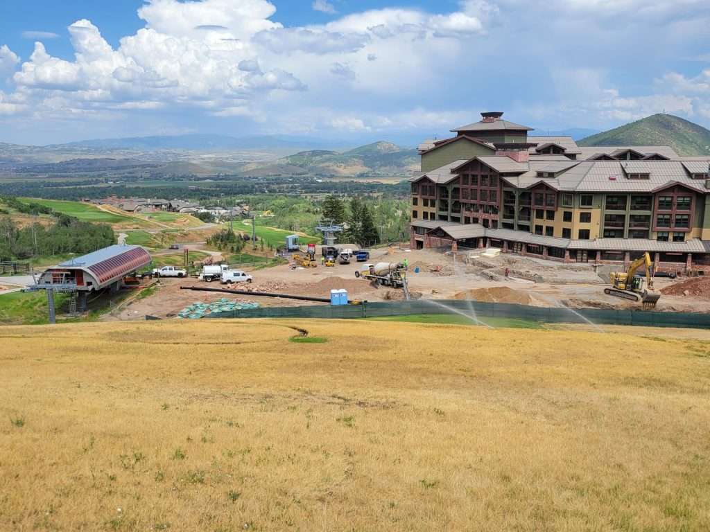 A large building under construction in a vast landscape with hills and cloudy sky.