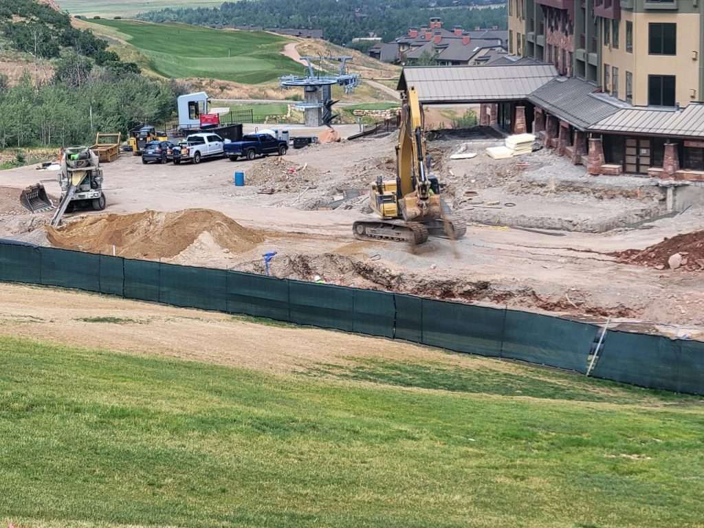 Construction site with heavy machinery and dirt piles near a building.