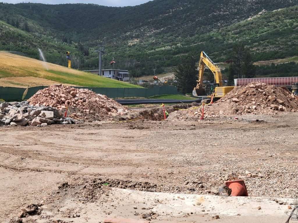 Construction site with excavator clearing rubble in a mountainous area.