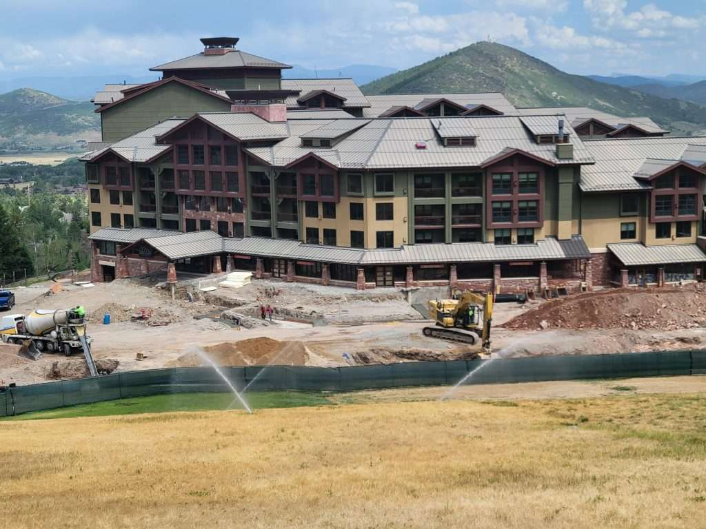 Large building under construction near a water body with sprinklers active.