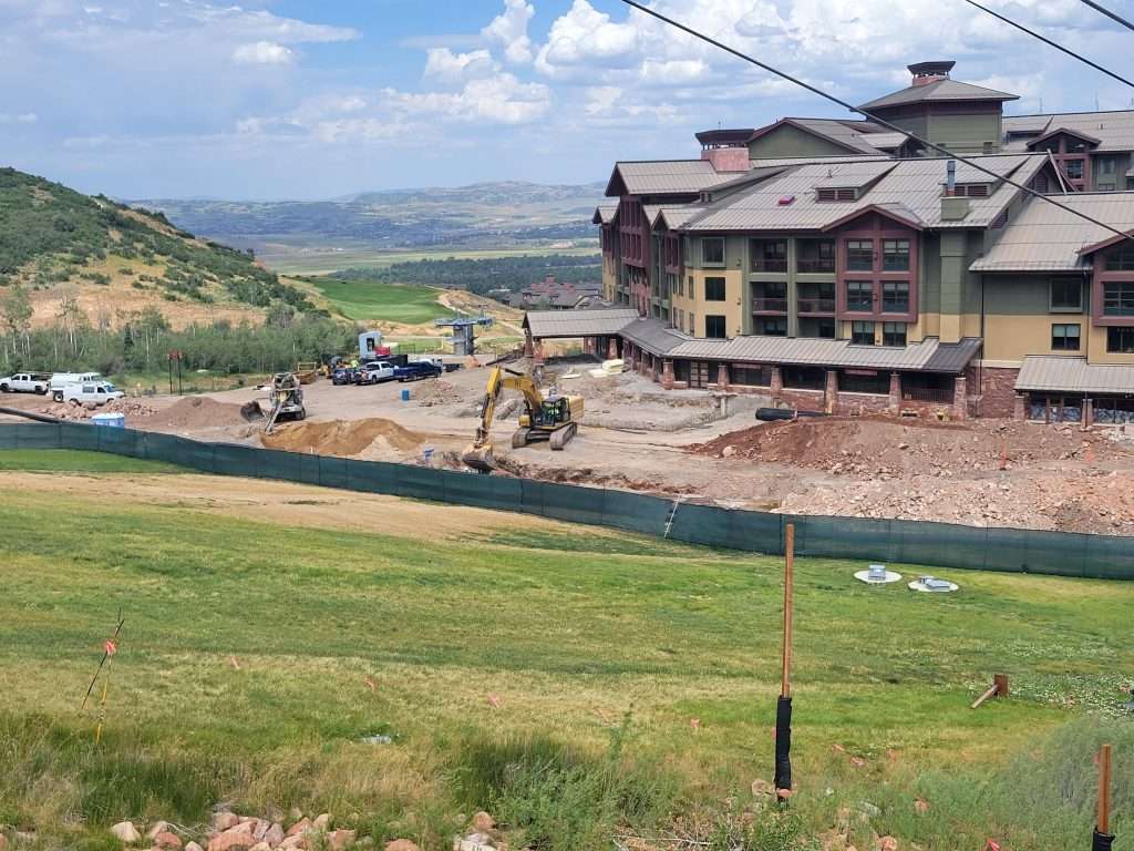 Construction site near a large building in a hilly area under a partly cloudy sky.