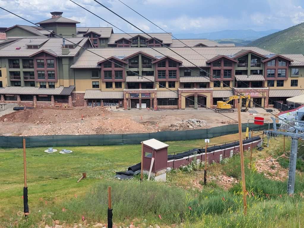 A large building under construction near a grassy area with mountains in the background.