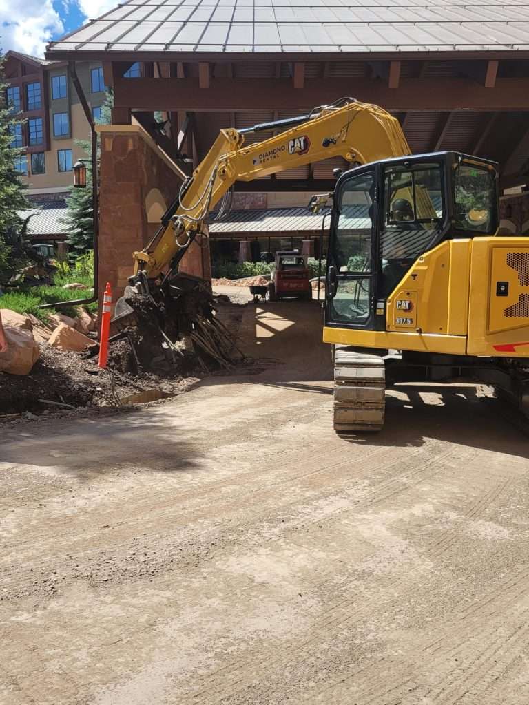 Yellow excavator digging at a construction site with dirt piles.