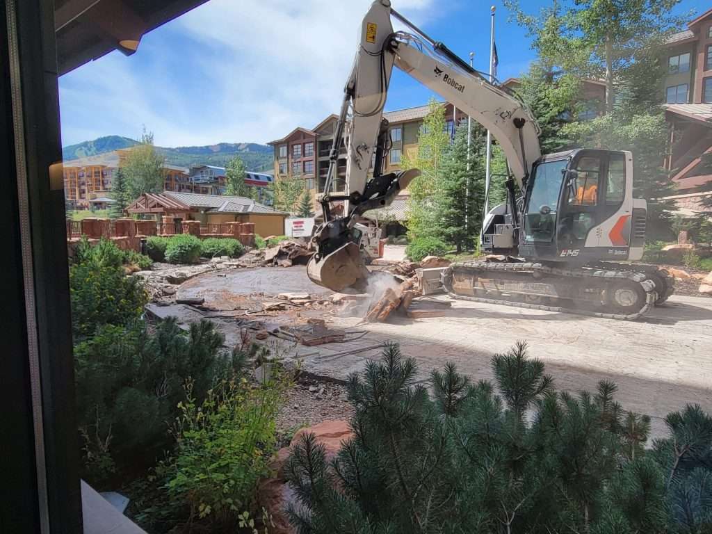 Excavator demolishes a building in a residential area on a clear day.