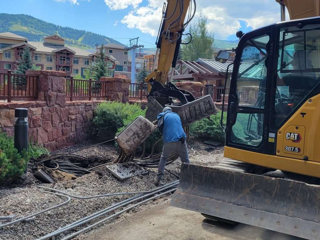 Worker clearing debris with excavator in a residential area.