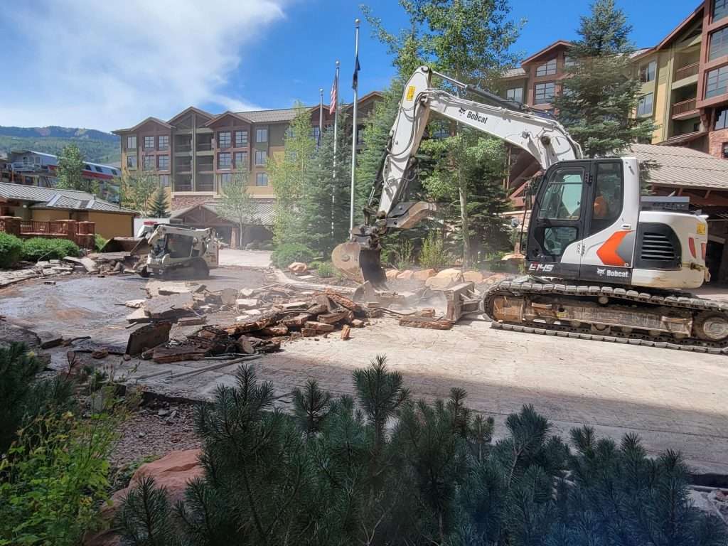 Excavator demolishing a building on a sunny day.