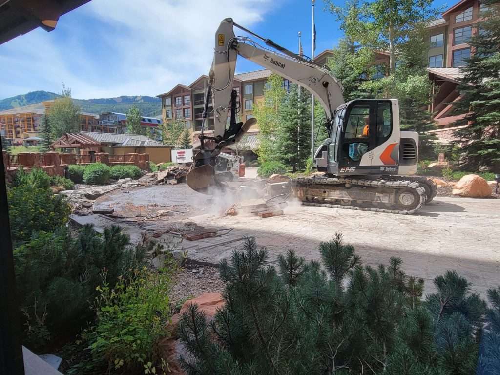 Excavator clearing a construction site with dust rising.