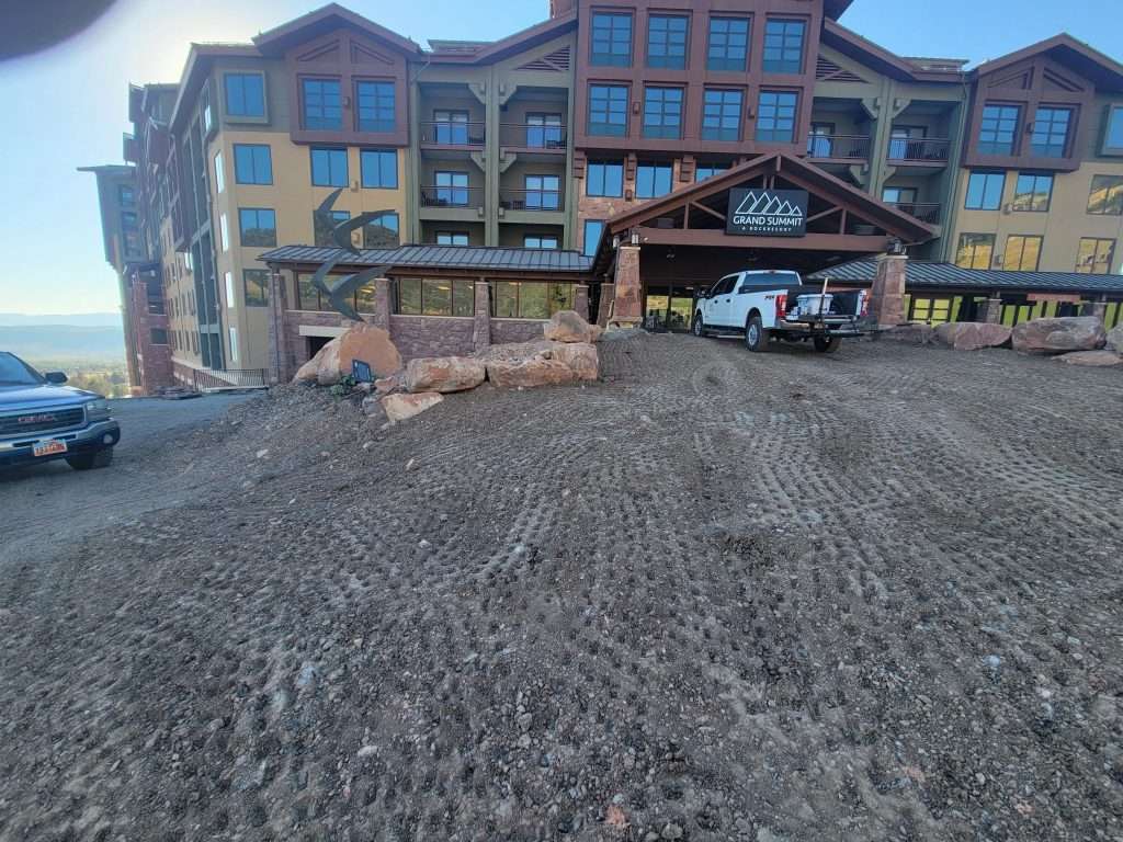 Construction site in front of a multi-story building with tire tracks on the ground.