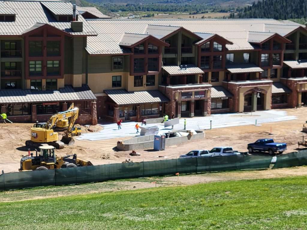 Construction site with buildings and heavy machinery near a grassy area.