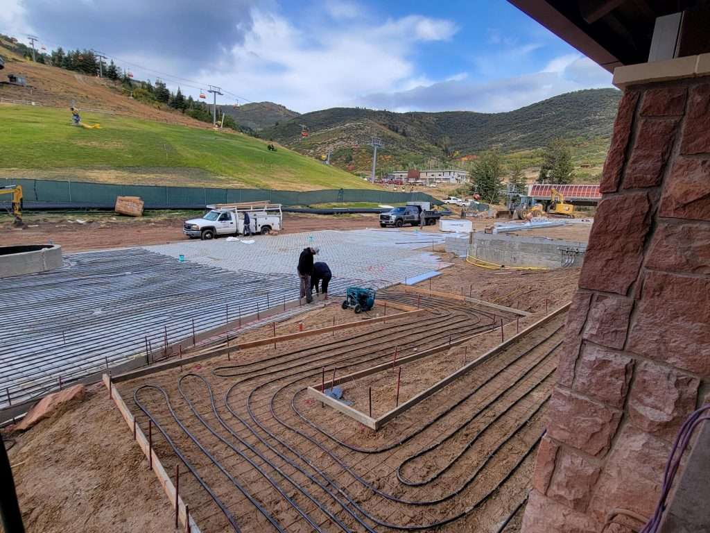 Workers preparing a patio area with coiled irrigation tubing in a scenic mountainous landscape.