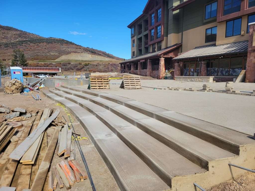 Construction site with concrete steps near a modern building under a mountainous backdrop.
