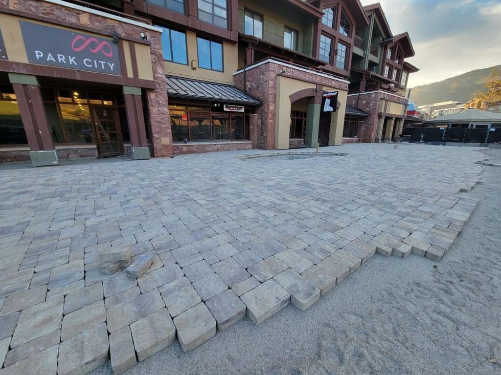 Construction site with cobblestone pavement being laid near a building.