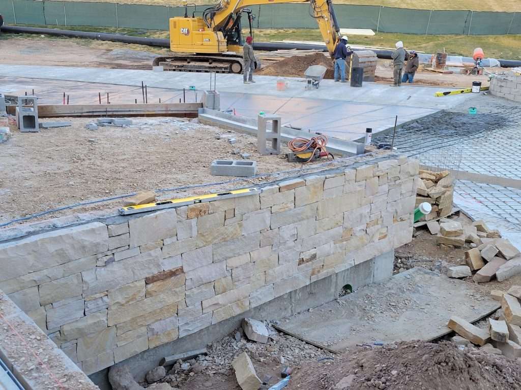 Construction site with stone foundation and excavator in background.
