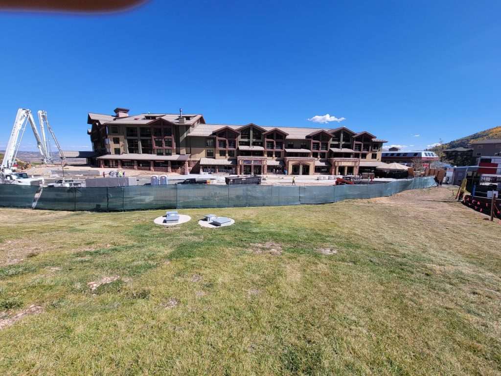 Large building under construction by a grassy area near water.