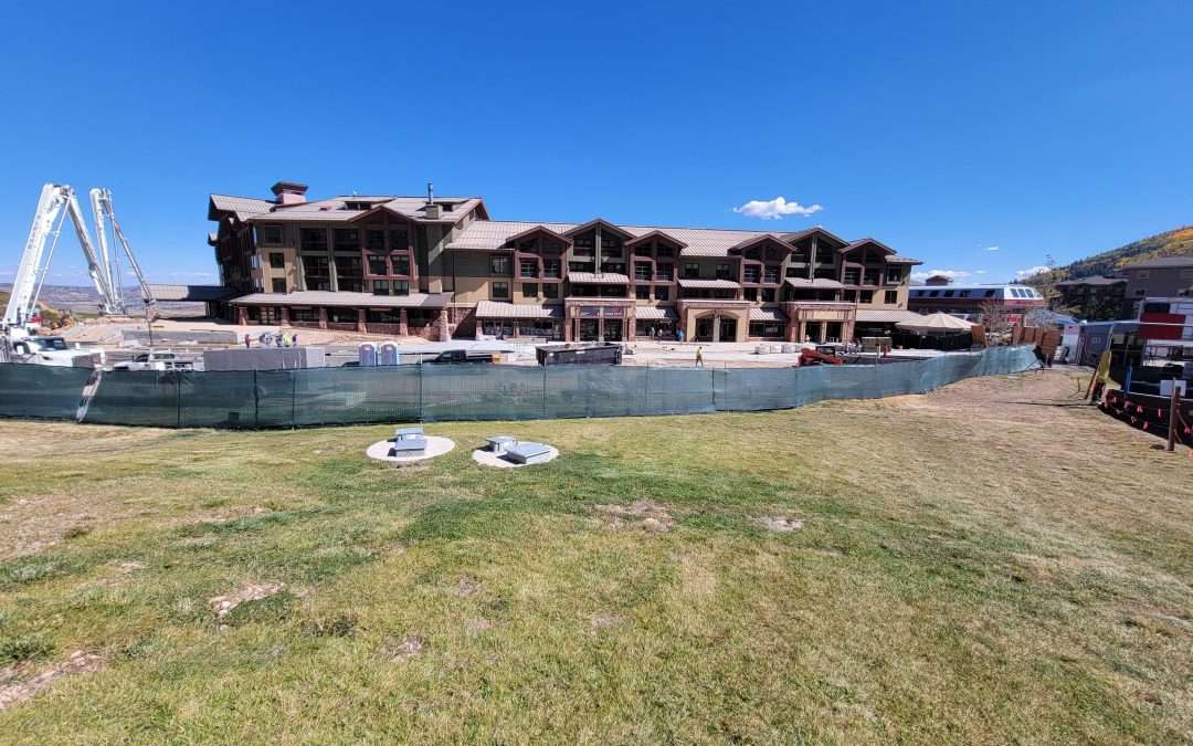 Large building under construction by a grassy area near water.