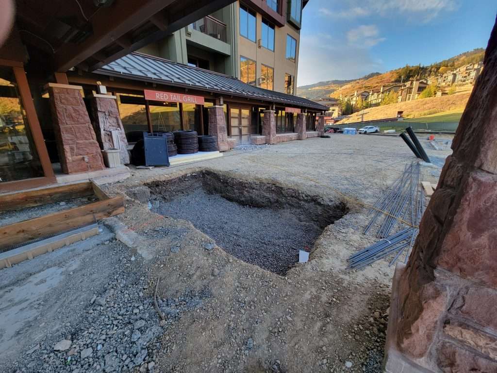 Excavation site near buildings revealing stone foundations under a clear sky.