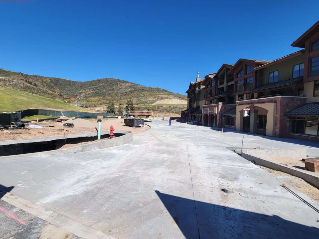 Construction site with concrete foundation and nearby buildings under clear blue sky.