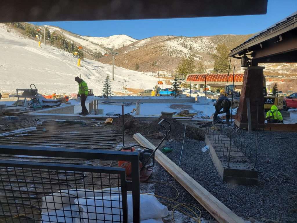 Workers preparing a snowy construction site with equipment and materials.