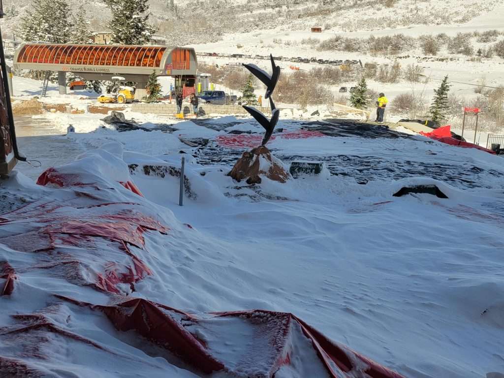 A snowy landscape with a partially covered tree and a building in the background.
