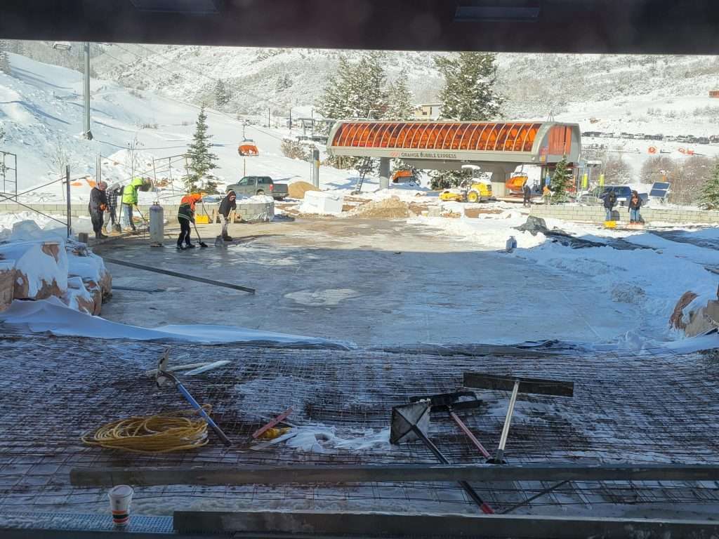 People working on a snowy road with a parked semi-truck nearby.