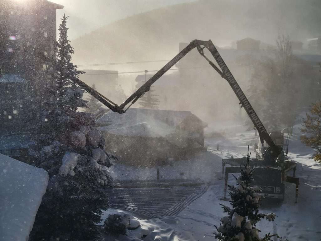Snow-covered mountain village with cranes and construction activity.