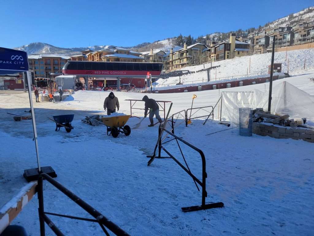 People and dogs in a snowy outdoor area with railings and buildings.