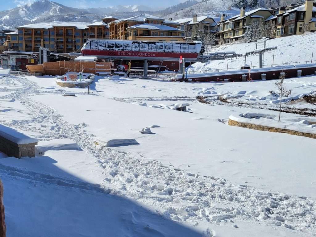 Snow-covered outdoor ice skating rink with buildings and mountains in the background.