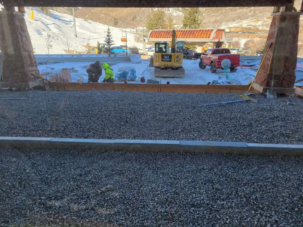 Workers operating heavy machinery at a construction site with gravel and dirt.
