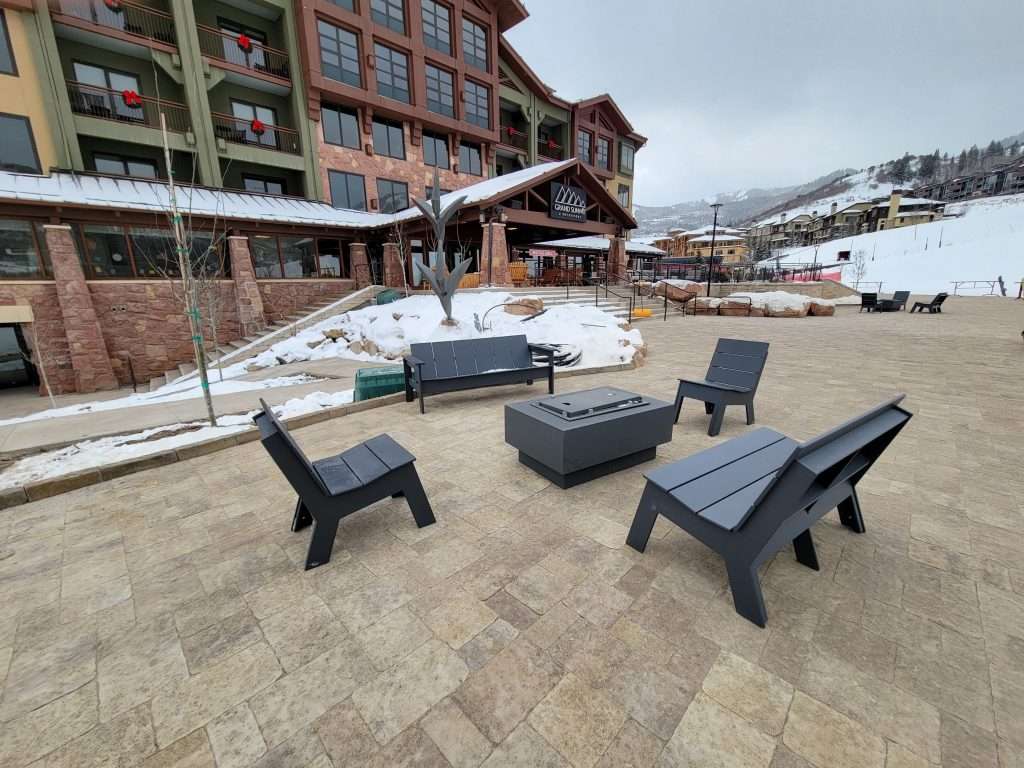 Outdoor seating area with black chairs and a stone fire pit in a snowy mountain resort.