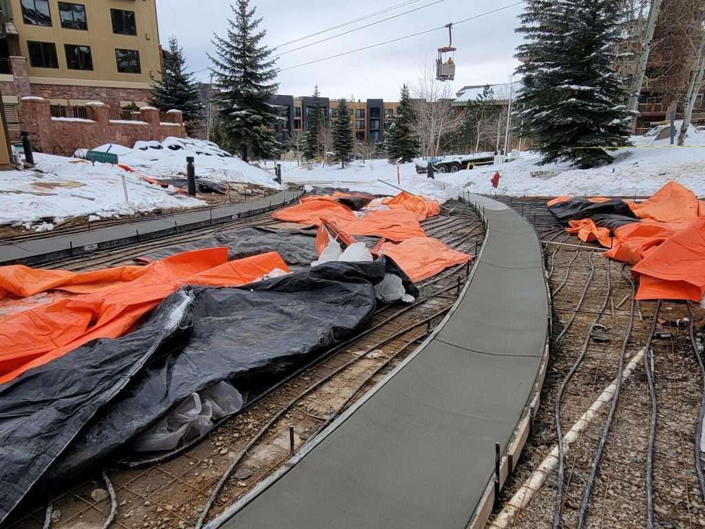 Newly poured concrete sidewalk in a snowy construction area.