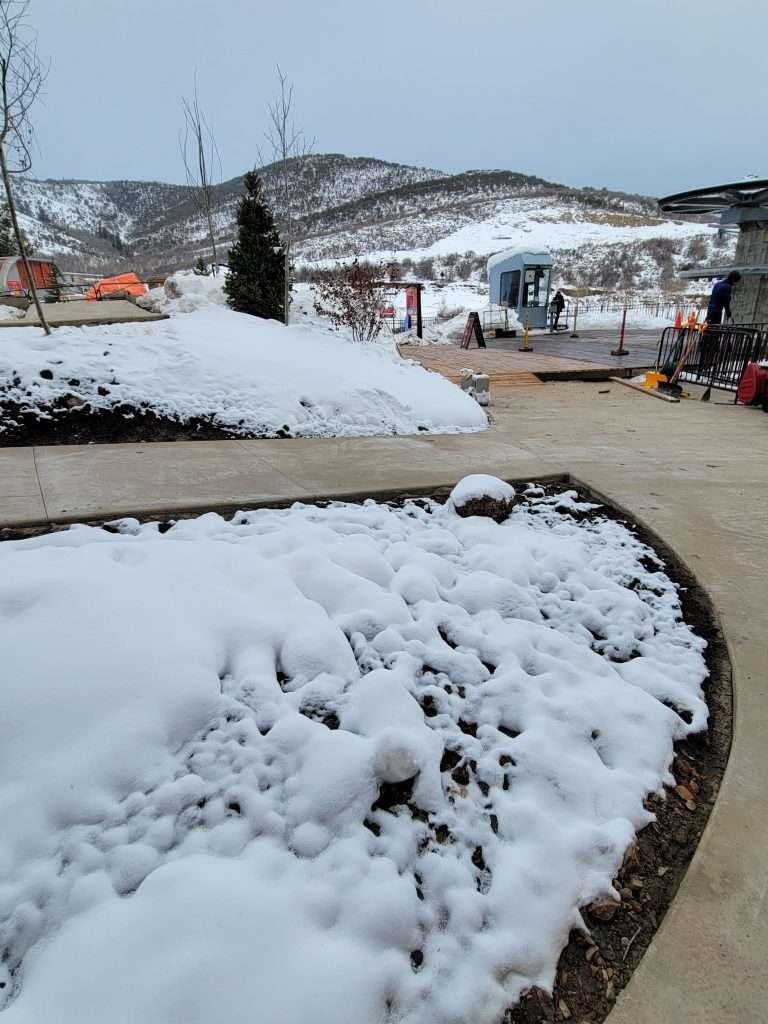 Snow-covered ground with a wooden structure and mountains in the background.