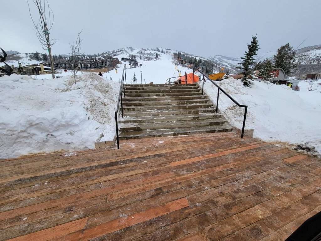 Snow-covered stairs with a ramp in a wintery outdoor setting.