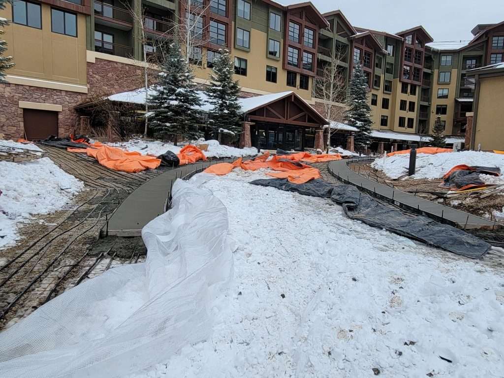 Snow-covered path leading to a lodge with orange fencing and buildings.