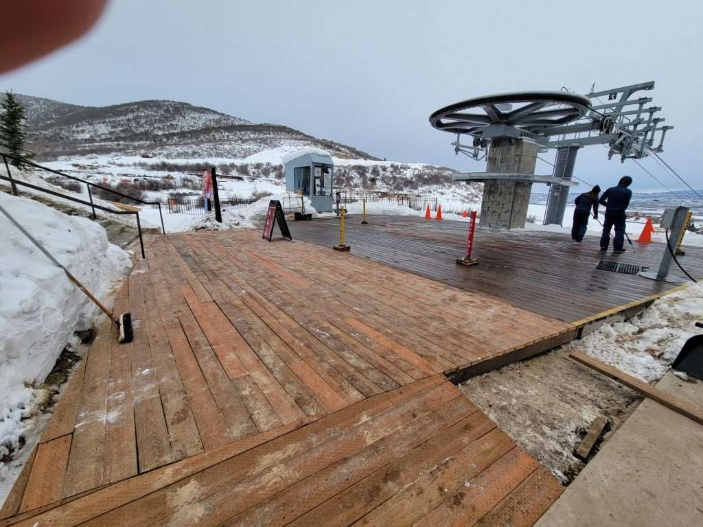 Wooden deck with people and snowy mountain view at a ski resort.