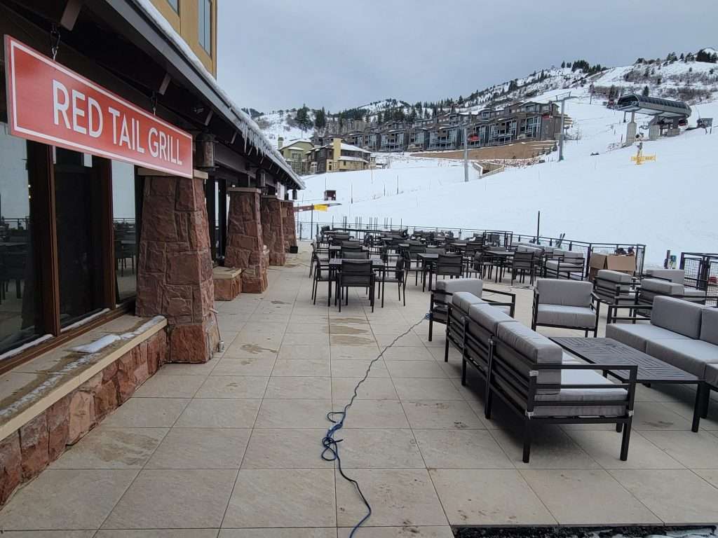 Outdoor seating area at a snowy mountain resort with empty tables and chairs.