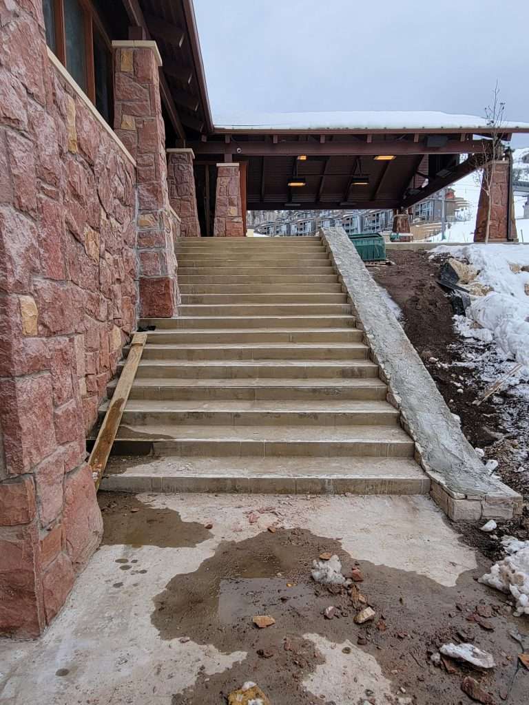 Concrete stairs between a red stone wall and a snowy slope.