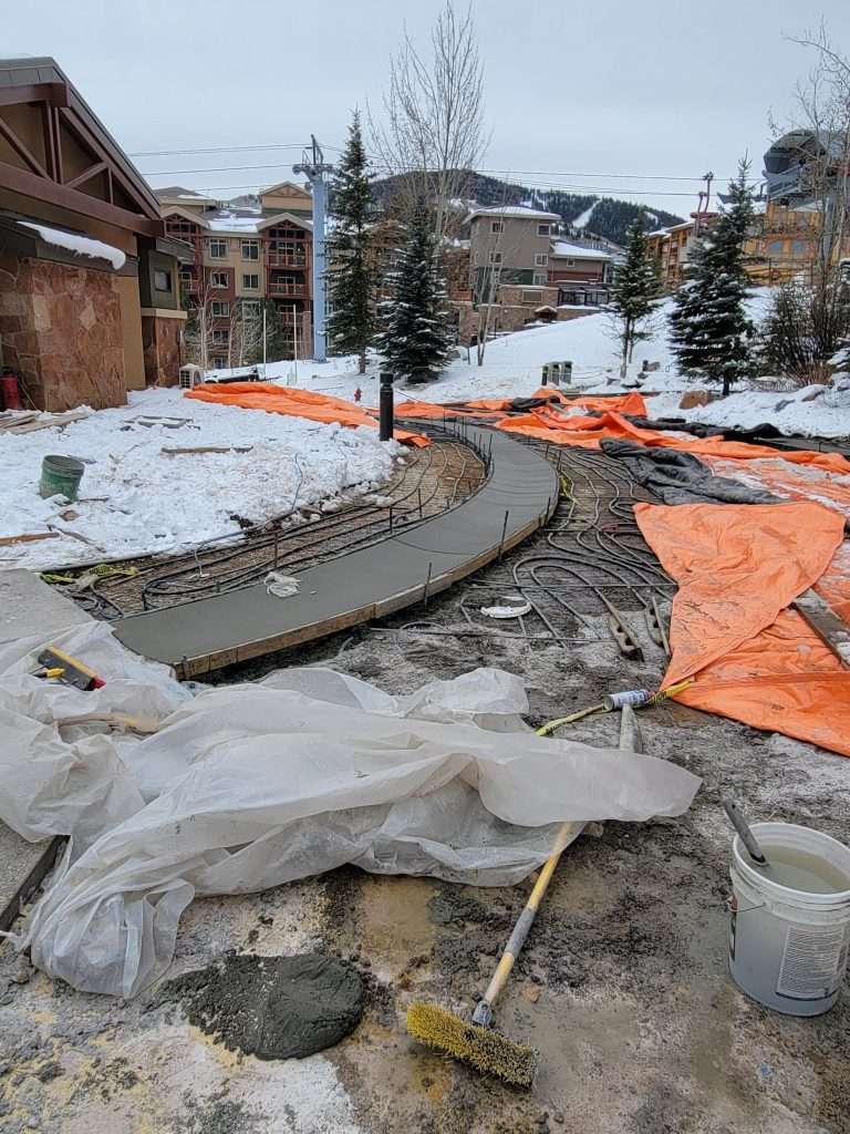 Construction site with curved concrete pathway and snow-covered surroundings.